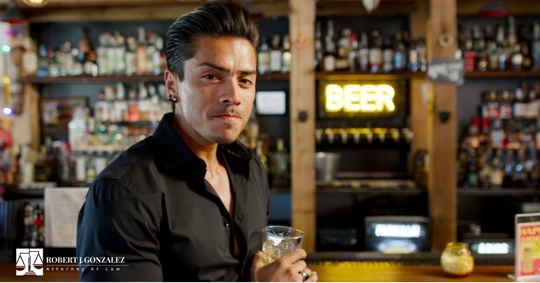 man with slicked back hair sipping on a drink at a bar counter